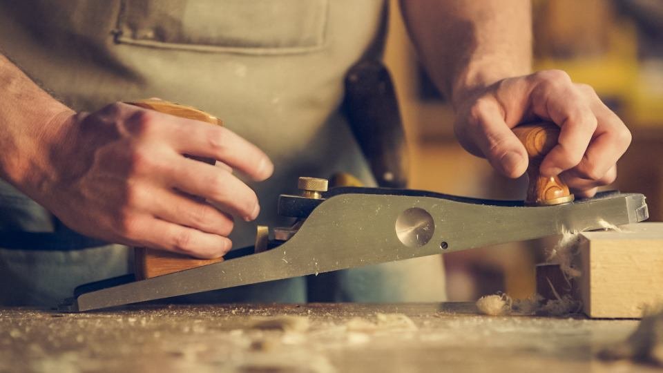 Mains d'un menuisier utilisant un rabot sur une planche de bois